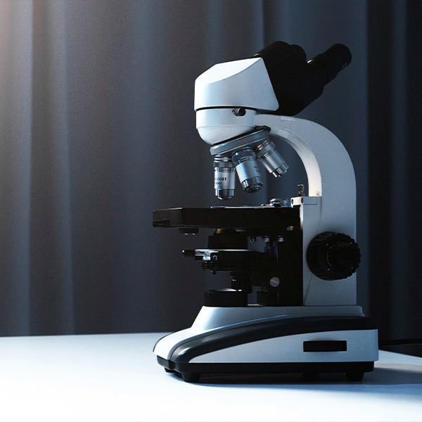 Close-up of a laboratory microscope placed on a white table with dark curtains in the background