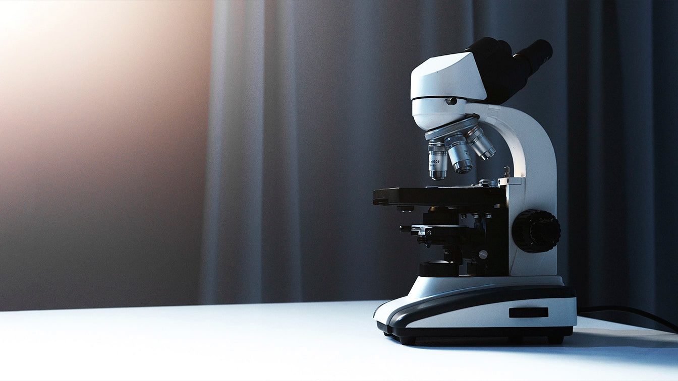 Close-up of a laboratory microscope placed on a white table with dark curtains in the background