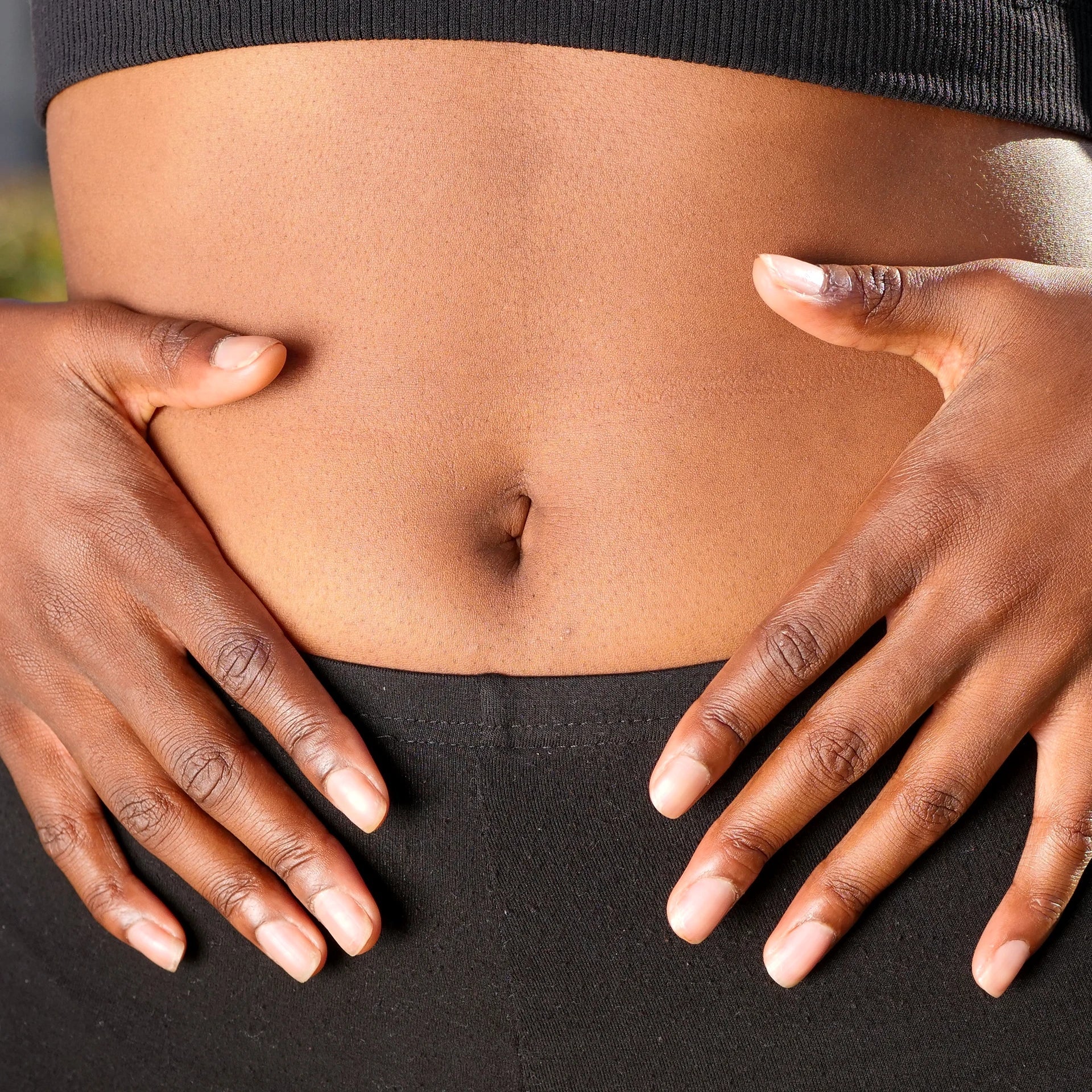 Close-up of a person’s midsection with hands gently resting on the stomach, symbolizing gut health and digestion