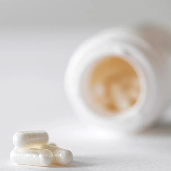 White capsules lying in front of an open supplement bottle, softly focused in a clean, minimalistic setting