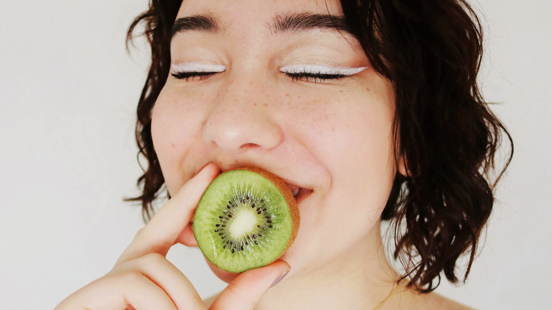Girl holding a kiwi over her mouth