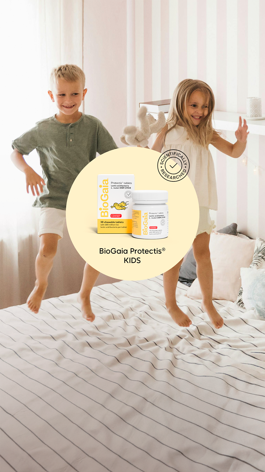 Two children jumping on a bed in a softly lit bedroom, with BioGaia Protectis Kids strawberry-flavoured tablets shown in a product callout