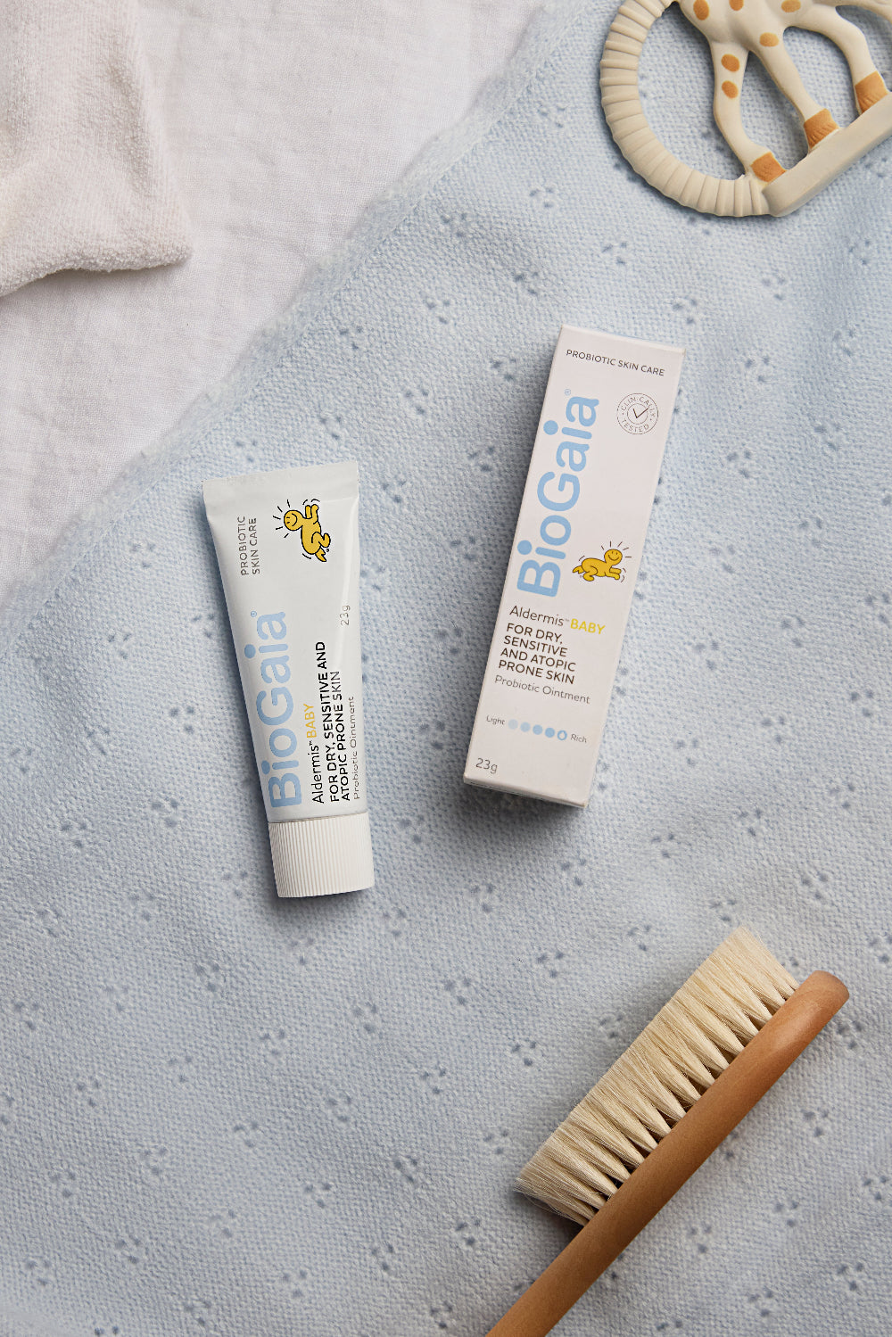BioGaia Skincare Probiotic Ointment tubes on a soft baby blanket with a wooden baby brush and teether.