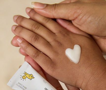 Mom and child hands holding BioGaia Aldermis Probiotic Ointment beside a heart-shaped dab of ointment on the skin. 