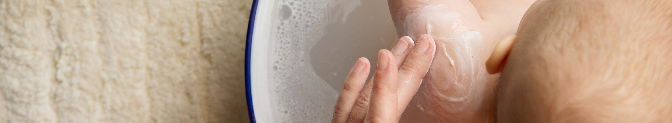 Baby taking a bath with milky water from the BioGaia Skincare Balm-to-Milk Body Wash and flowers in the water.