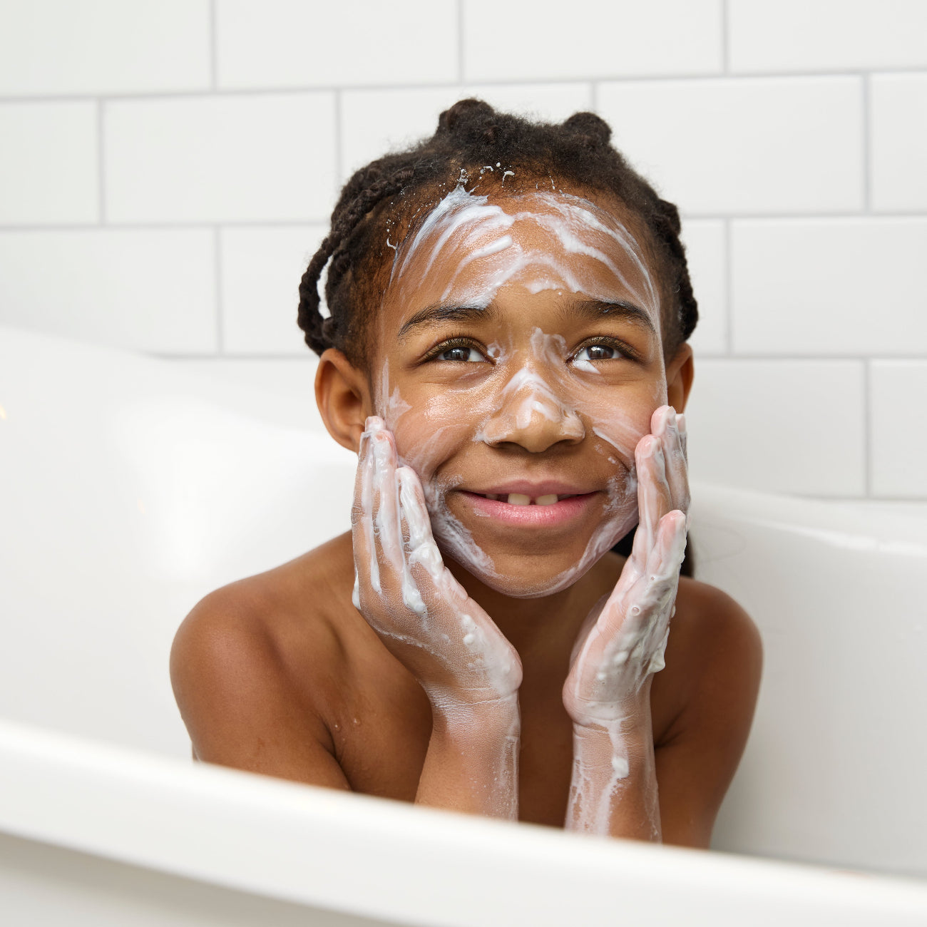 Child applying Biogaia Skincare Balm-to-Milk wash to her face with white milky texture in bathtub.