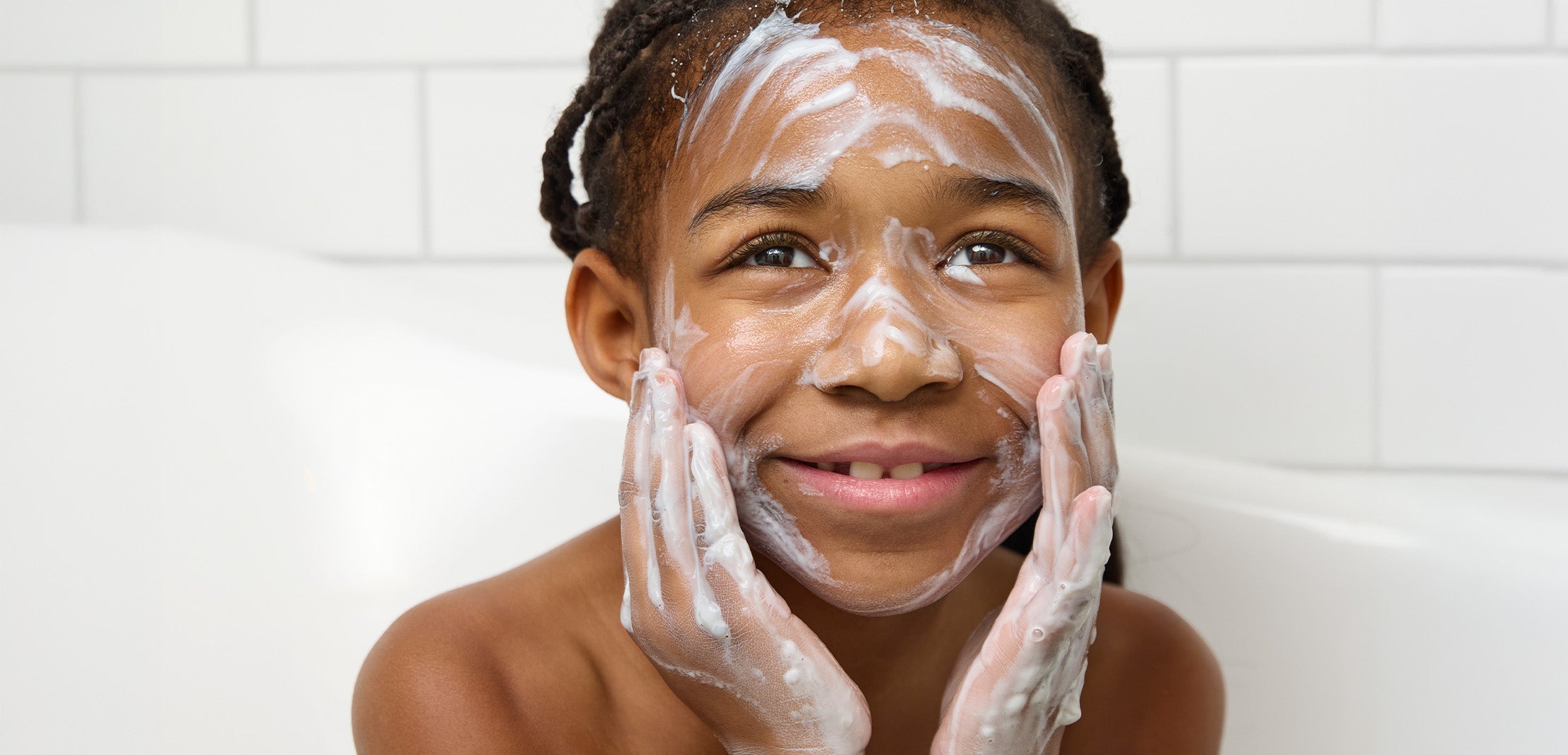 Child applying Biogaia Skincare Balm-to-Milk wash to her face with white milky texture in bathtub.