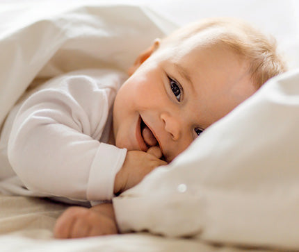 Smiling baby lying on a white blanket with a soft focus background