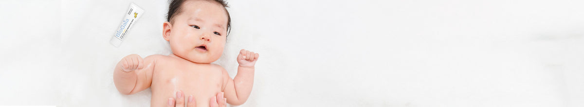 Close-up of a baby with mother's hands on a white background applying BioGaia Skincare Aldermis Probiotic Ointment.