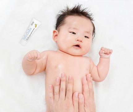 Close-up of a baby with mother's hands on a white background applying BioGaia Skincare Aldermis Probiotic Ointment.