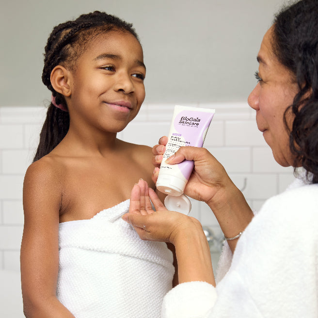 Mother applying BioGaia Skincare Soothing Face & Body Lotion to her child while the two smile at each other in white towels in a bathroom setting.