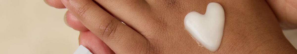 Mom and child hands holding BioGaia Aldermis Probiotic Ointment beside a heart-shaped dab of ointment on the skin. 