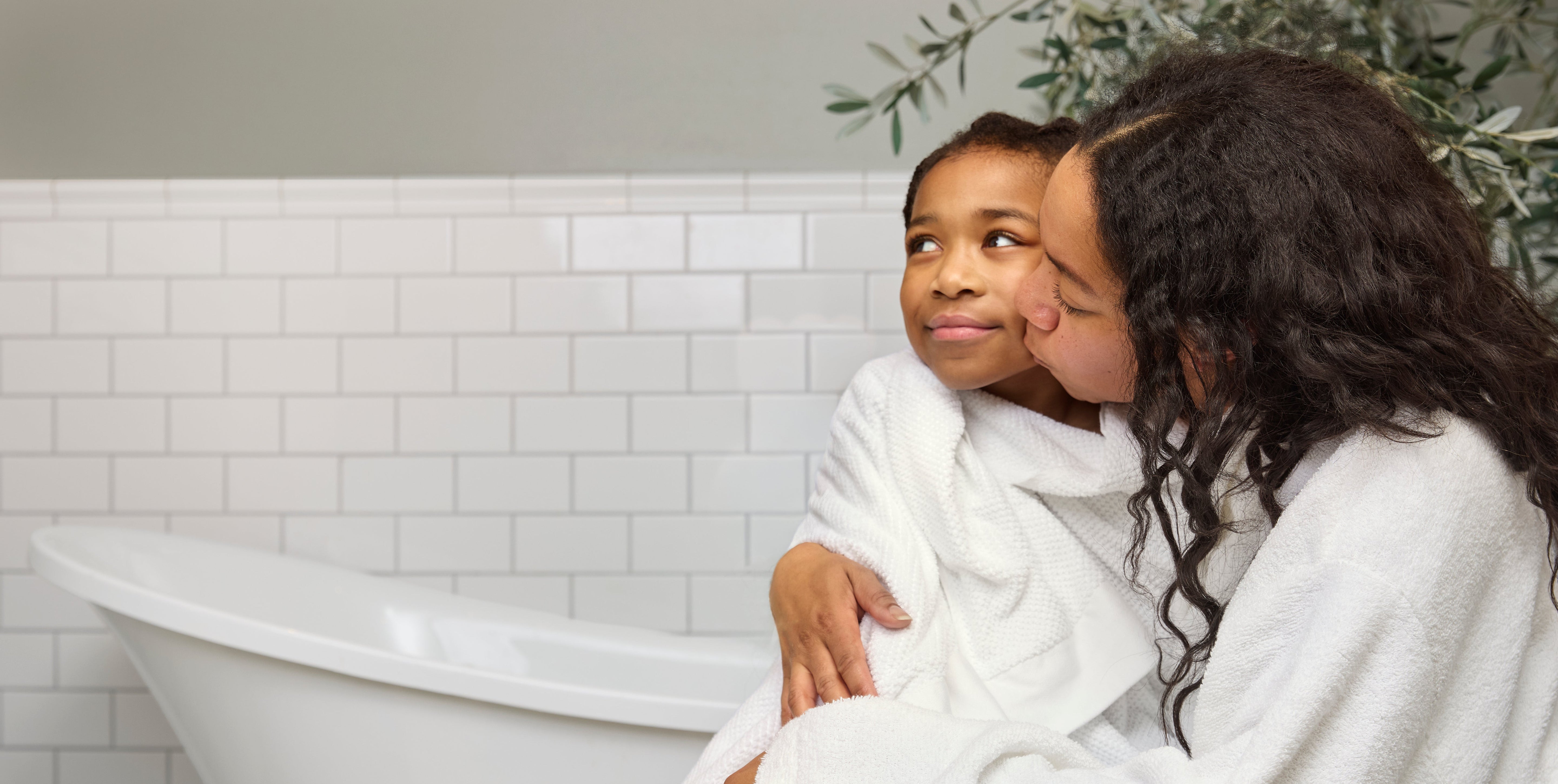 Mom kissing a child on the cheek with a white tiled wall in the background.