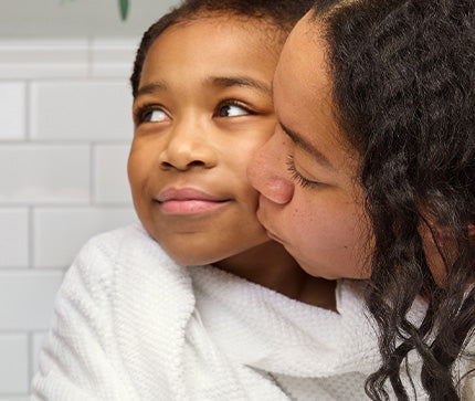 Mom kissing a child on the cheek with a white tiled wall in the background.