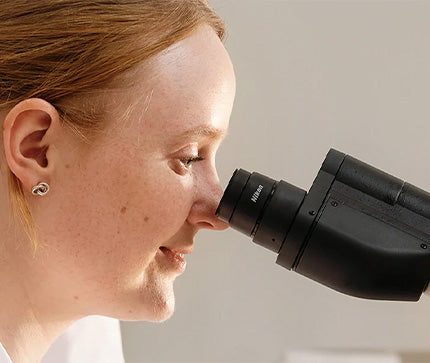 Researcher looking through a microscope, representing BioGaia Skincare’s science-backed approach to delicate skin care.