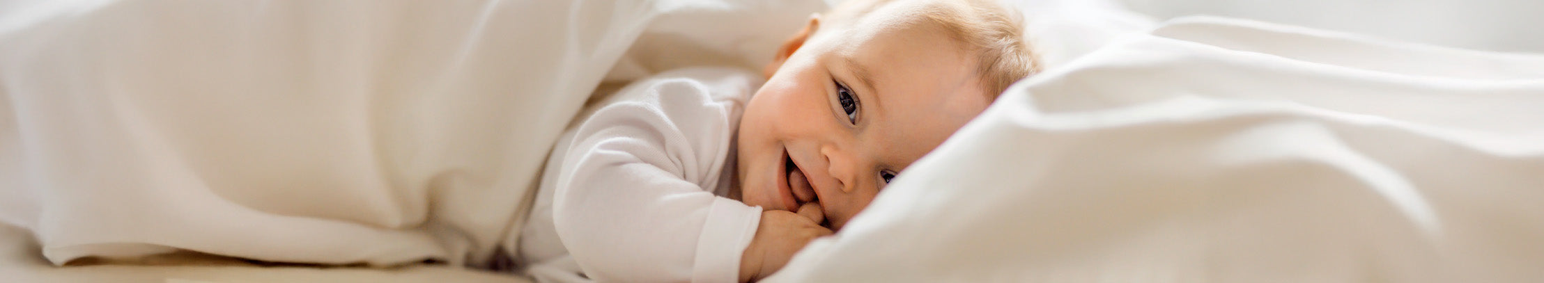 Smiling baby lying on a white blanket with a soft focus background